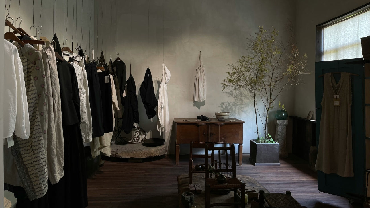 Lojas Vibe – Minimalist clothing boutique interior with neutral-toned garments hanging on display, wooden furniture, and natural decor creating a calm and stylish atmosphere.